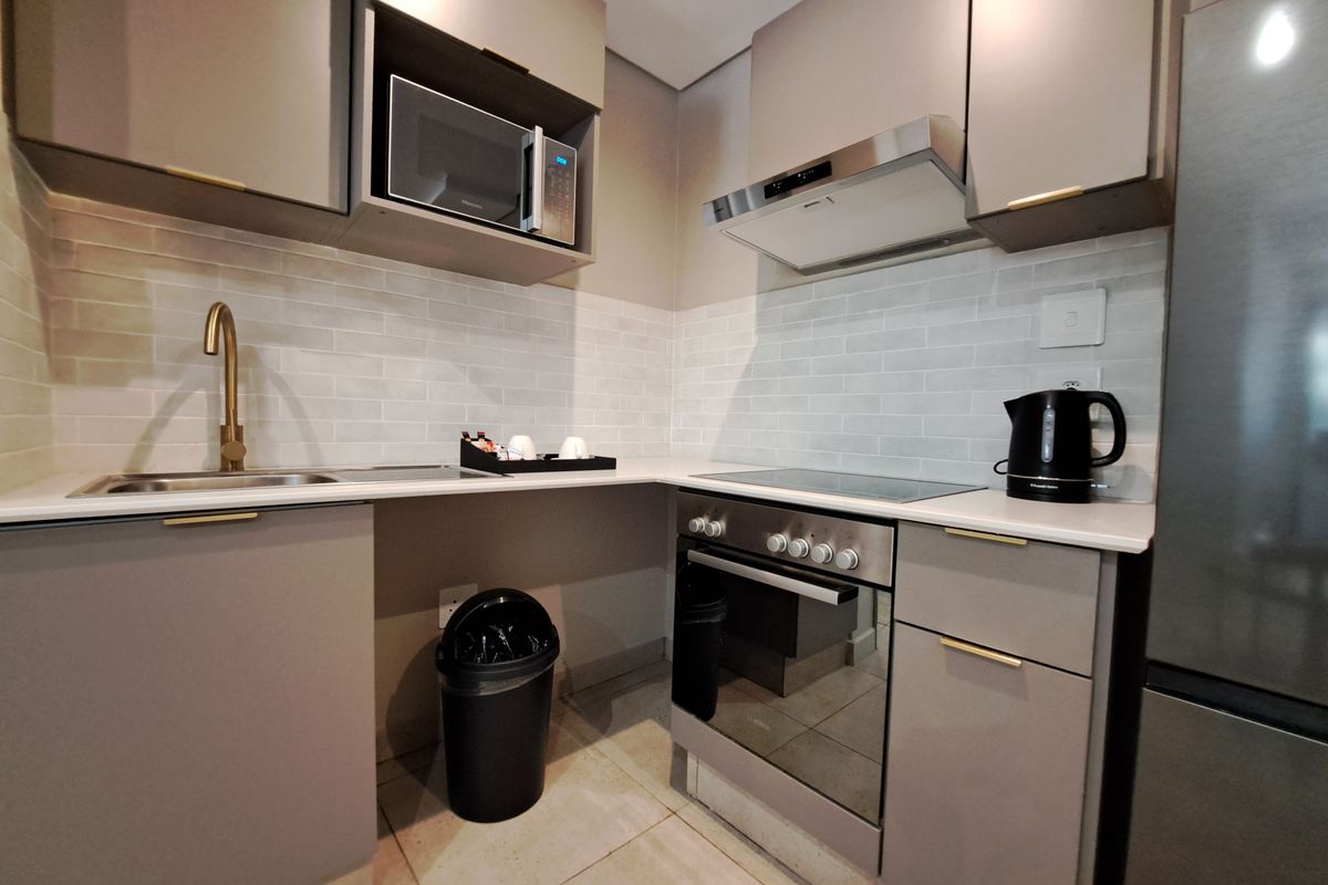 Modern kitchen featuring sleek grey cabinetry, stone countertops, subway tile backsplash, and integrated stainless steel appliances including an oven and extractor fan.