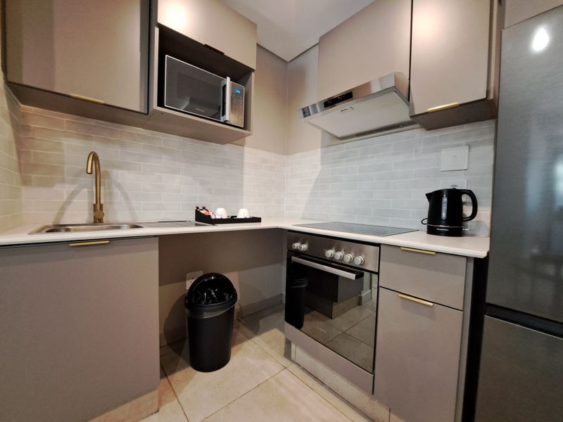 Modern kitchen featuring sleek grey cabinetry, stone countertops, subway tile backsplash, and integrated stainless steel appliances including an oven and extractor fan.