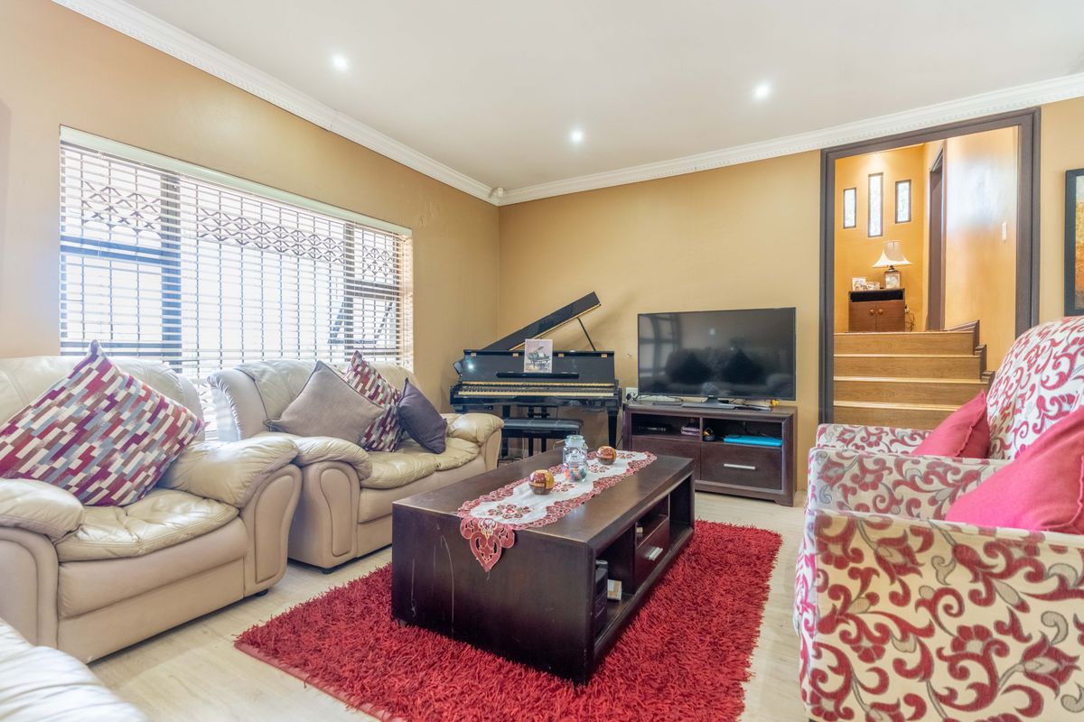 A comfortable living room featuring crown molding, recessed lighting, and large windows with security shutters, leading to an adjacent staircase.