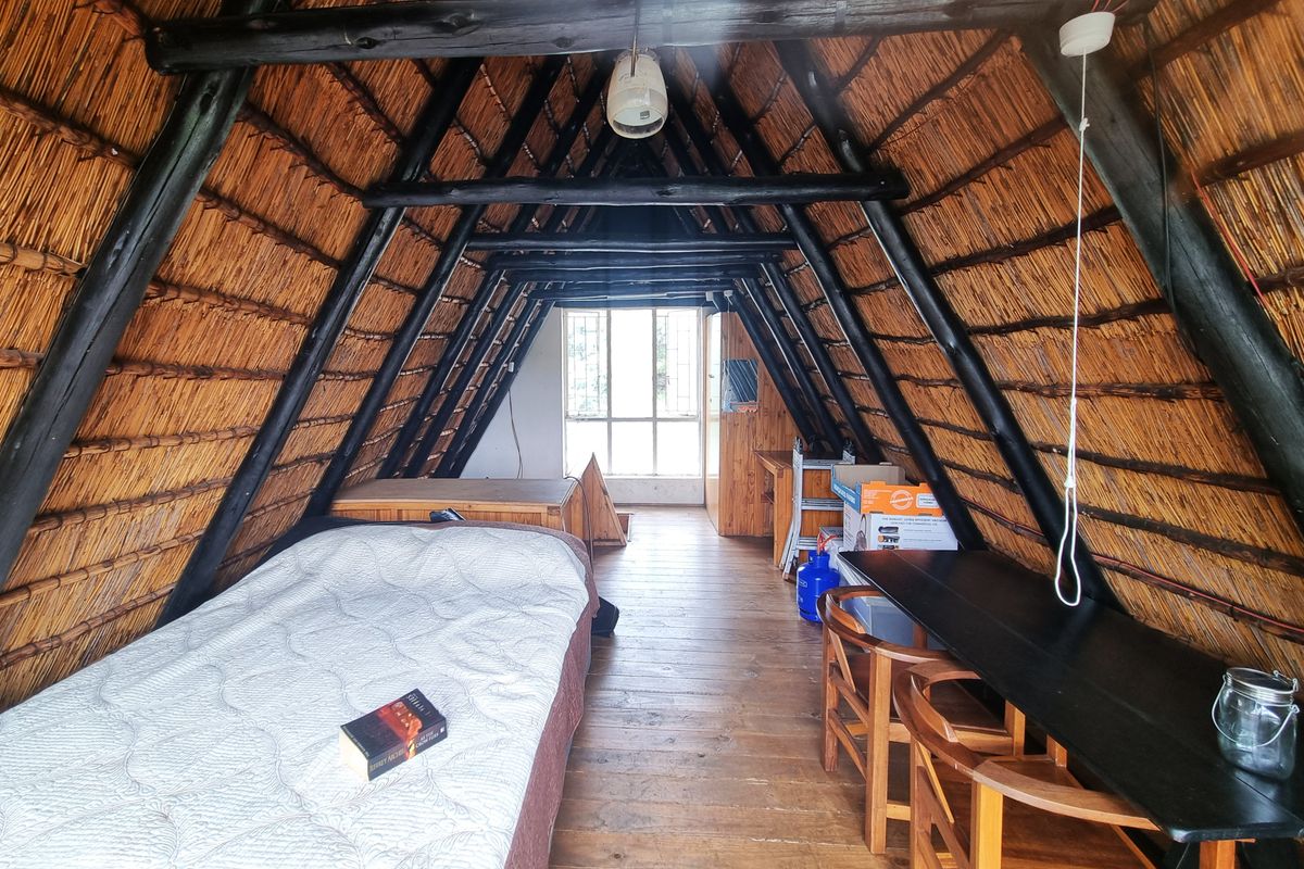 A rustic bedroom featuring a distinctive A-frame design with exposed timber rafters and a thatched roof, complemented by timber flooring and natural light.