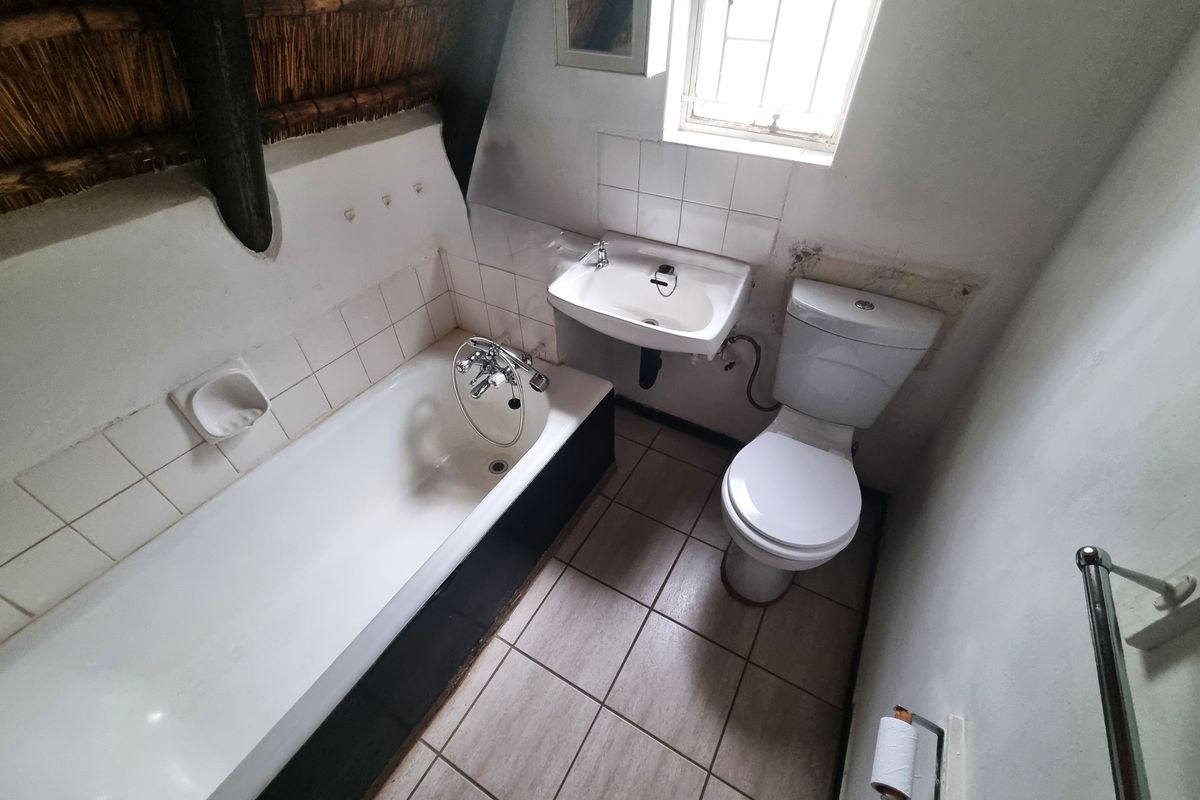 A compact bathroom featuring a bathtub, washbasin, and toilet, with tiled flooring and a distinctive thatched roof ceiling.