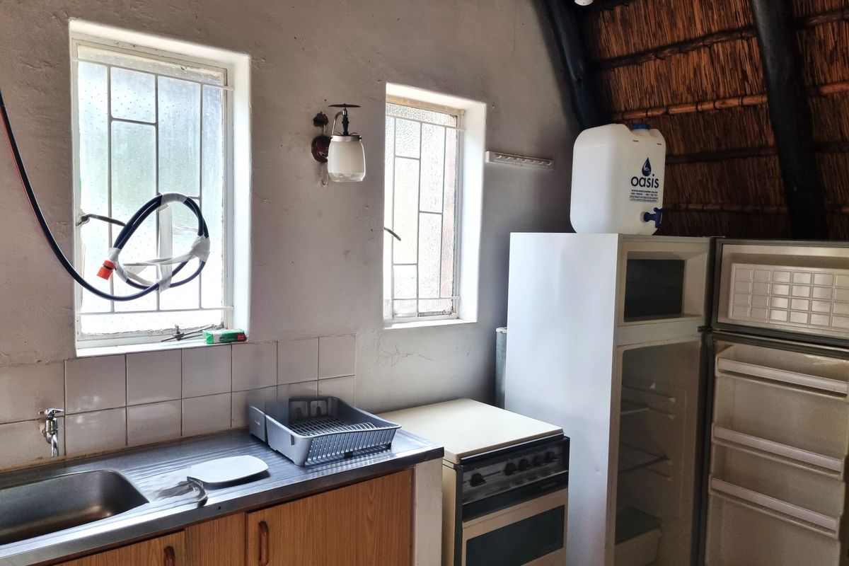 A rustic kitchen area featuring a stainless steel sink, tiled splashback, and a thatched roof ceiling with exposed timber beams.