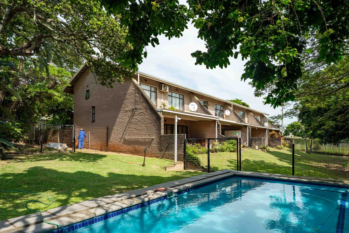 Rear view of a townhouse complex featuring a private swimming pool, brick exterior walls, and a shared garden area.