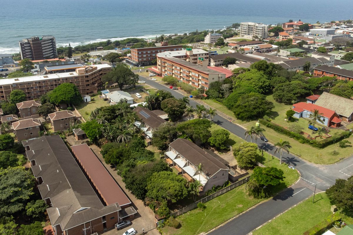 An aerial view of the townhouse complex and surrounding neighbourhood, showcasing the proximity to the coastline and established residential infrastructure.