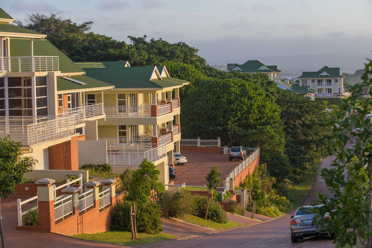 An elevated view of a residential estate featuring multi-story buildings with green roofs, paved driveways, and landscaped surroundings.