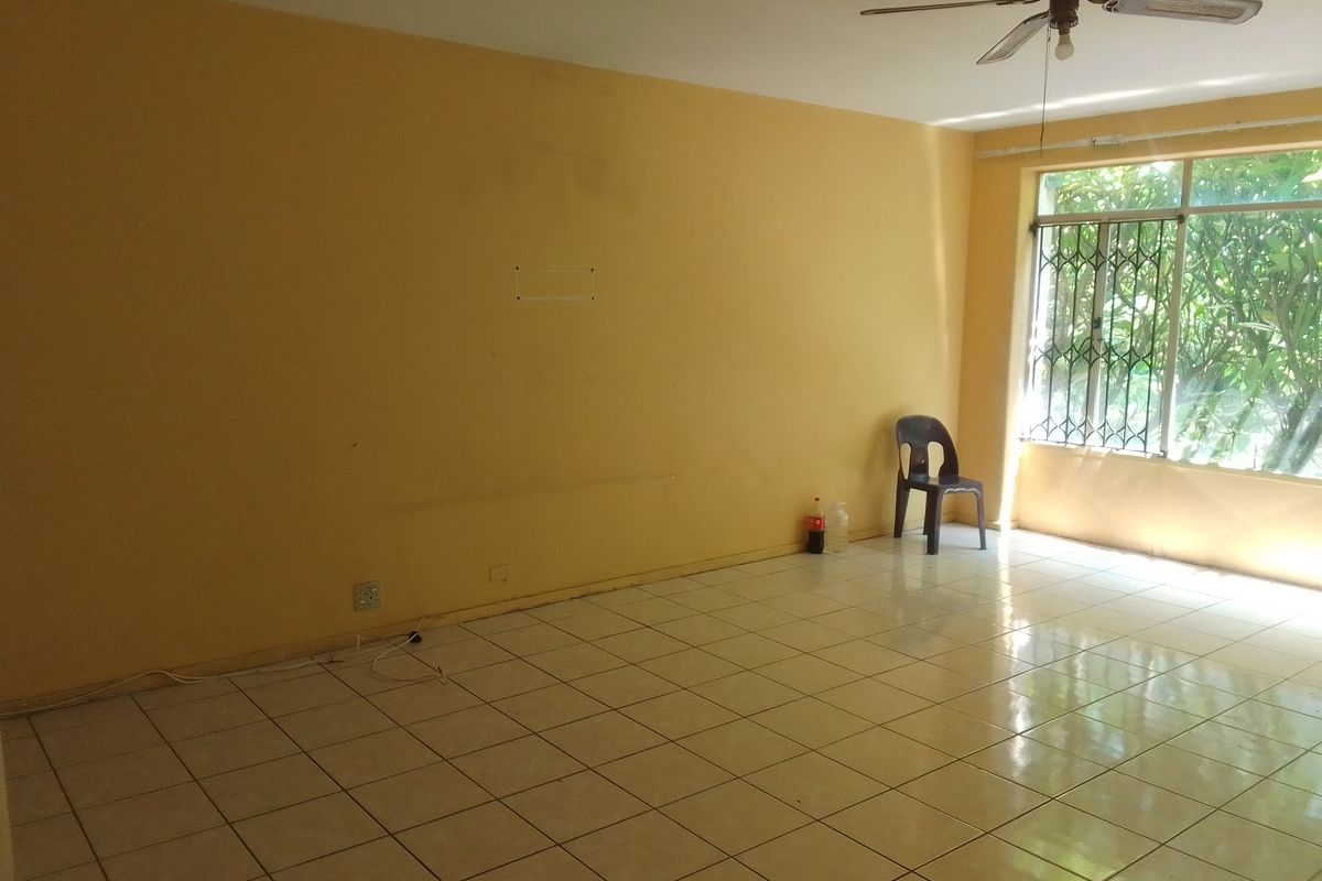 An empty living room featuring tiled flooring, a ceiling fan, and a large window with security bars, offering a blank canvas for renovation.