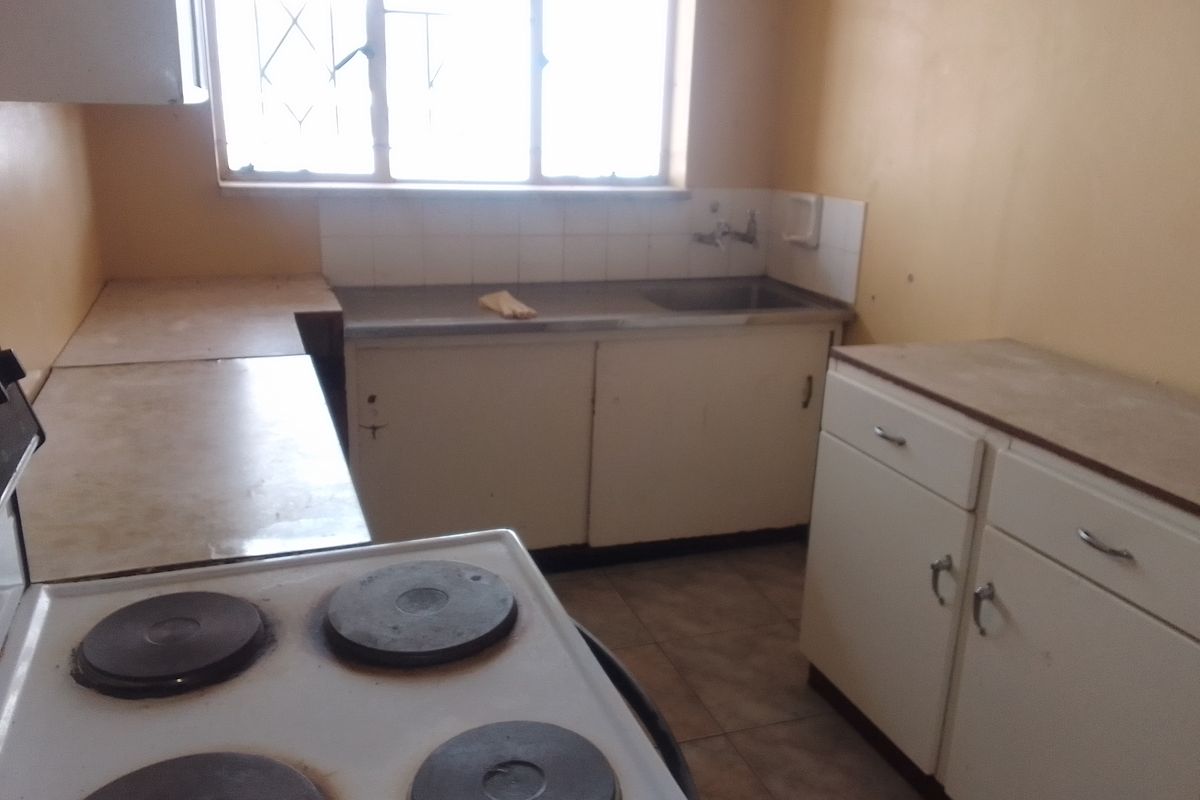 A dated kitchen featuring original cabinetry, a stainless steel sink, and an electric stove, requiring cosmetic updates to modernize the space.