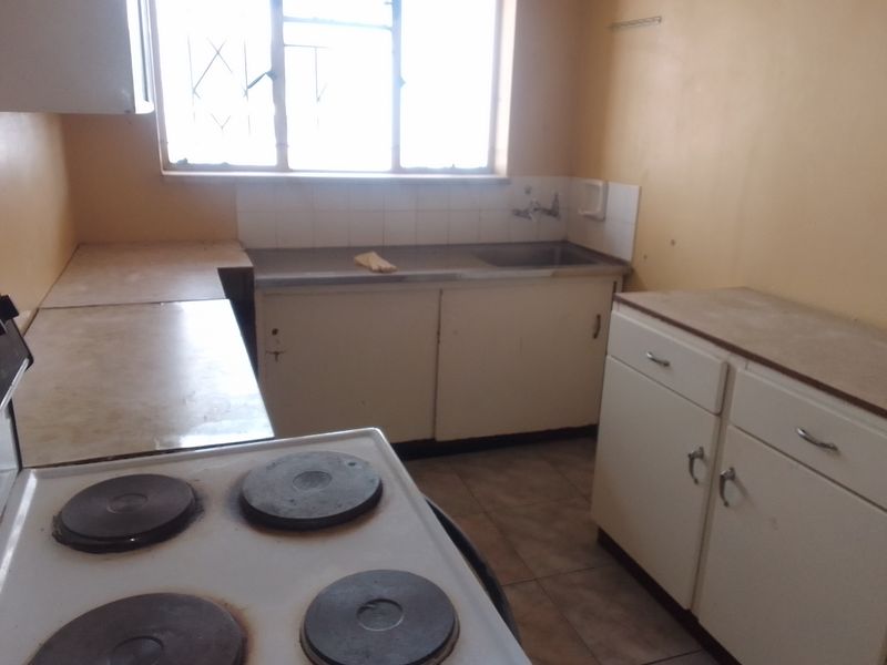 A dated kitchen featuring original cabinetry, a stainless steel sink, and an electric stove, requiring cosmetic updates to modernize the space.