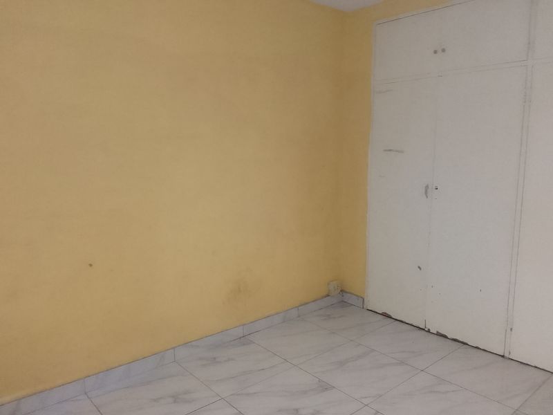 An empty bedroom featuring tiled flooring and a built-in wardrobe, requiring cosmetic updates to the walls and cabinetry.