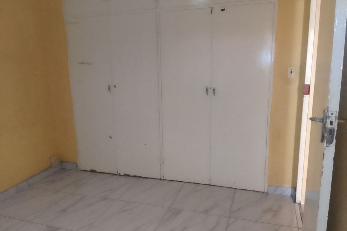 An empty bedroom featuring tiled flooring and built-in cupboards with visible signs of wear and tear.