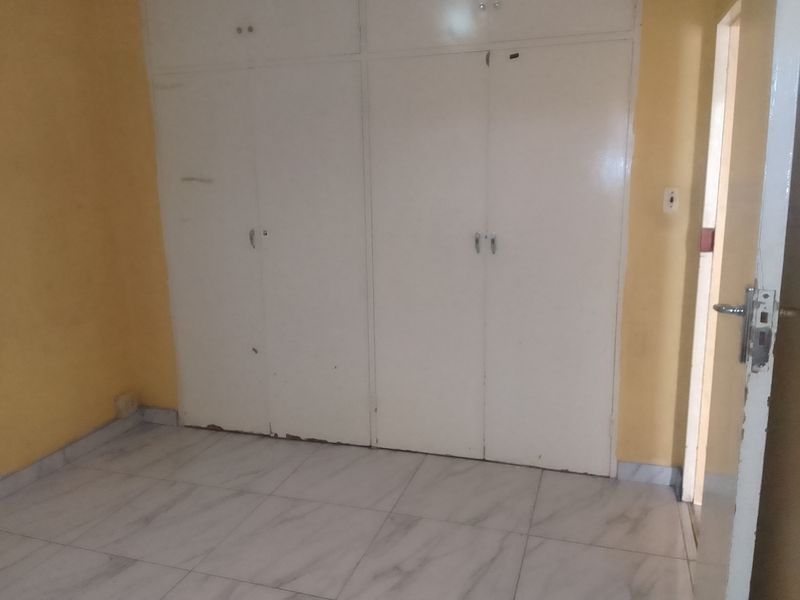 An empty bedroom featuring tiled flooring and built-in cupboards with visible signs of wear and tear.