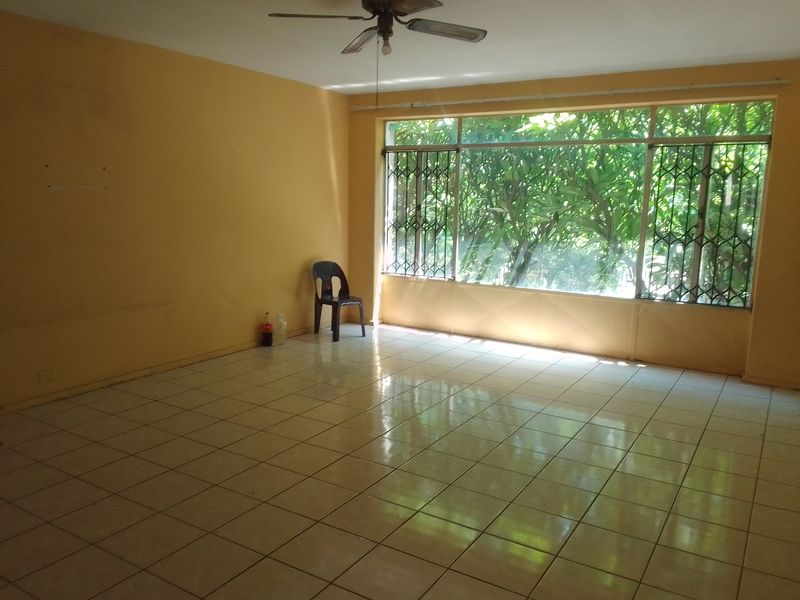 Spacious living area featuring large windows with security bars, tiled flooring, and a ceiling fan, offering a blank canvas for interior design.