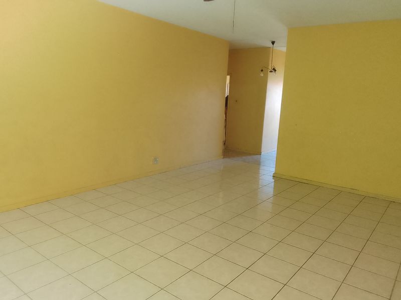An empty living room featuring yellow painted walls and light-colored ceramic floor tiles, offering a blank canvas for potential interior design updates.