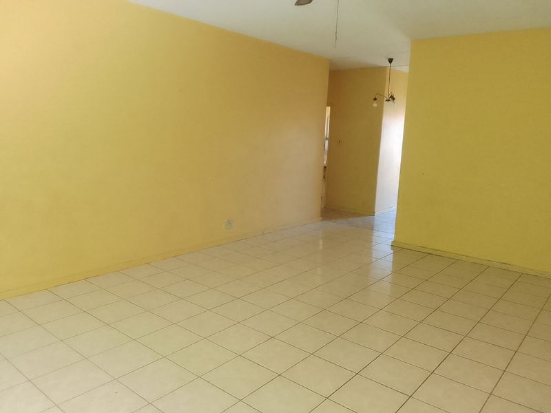 An empty living area featuring ceramic tile flooring, yellow painted walls, and a ceiling fan, offering a blank canvas for potential renovation.