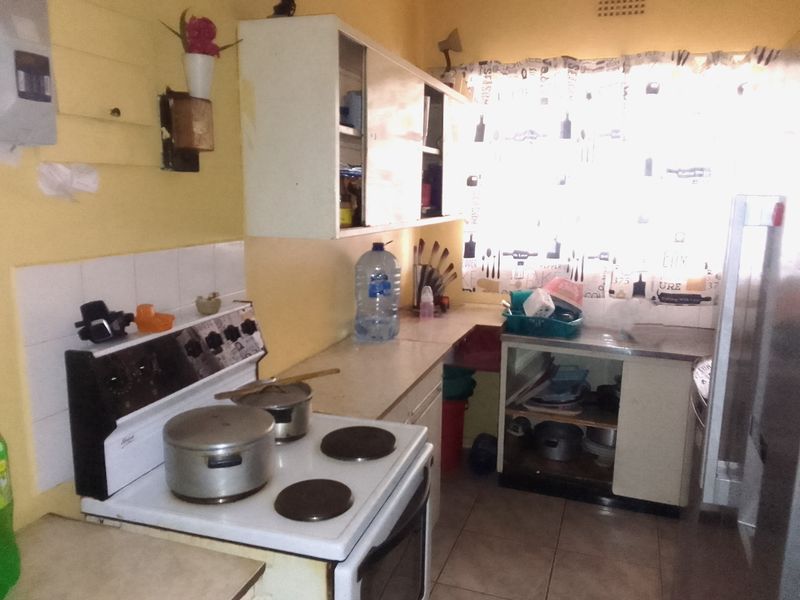 A dated kitchen featuring an electric stove, tiled backsplash, and basic cabinetry. The space would benefit from modern updates and improved lighting.