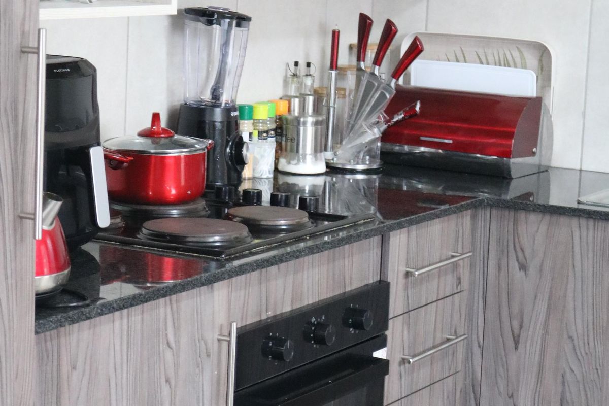 A compact kitchen featuring modern wood-grain cabinetry, granite countertops, a built-in oven, and an electric hob with an overhead extractor fan.