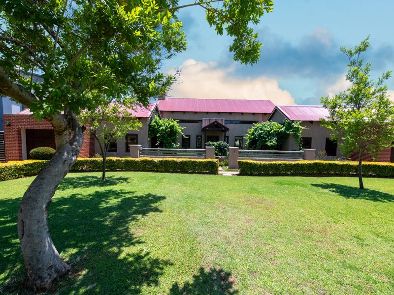 A well-maintained front exterior view of a house featuring a metal roof, brick facade, and a neatly landscaped garden with established hedging.
