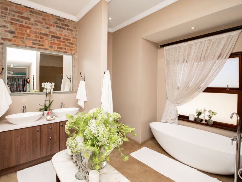 Modern bathroom featuring a double vanity with vessel sinks, a freestanding bathtub, and an exposed brick feature wall with a large mirror.