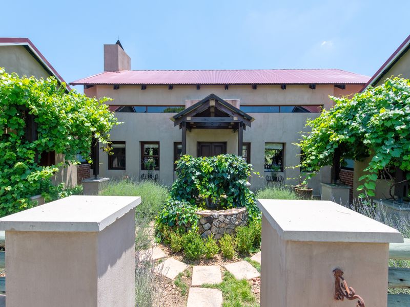Front facade of a residence featuring a metal roof, timber entrance canopy, and a central stone-clad fountain surrounded by landscaped garden beds.