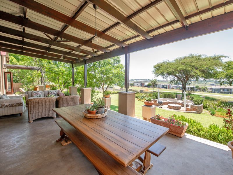 Spacious covered patio featuring exposed timber beams and concrete flooring, overlooking a landscaped garden with a built-in fire pit and scenic views.