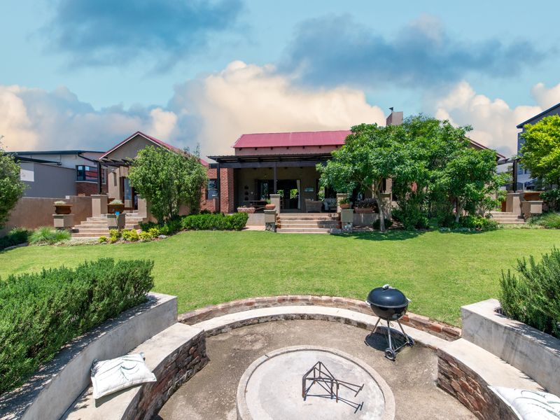 Spacious rear garden featuring a built-in circular fire pit, manicured lawn, and a covered patio area attached to the main residence.