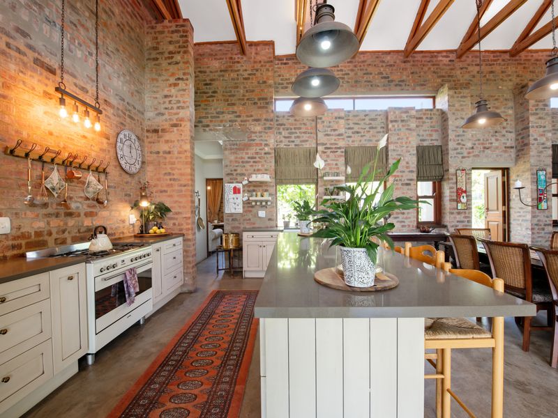 Spacious kitchen featuring exposed brick walls, timber ceiling beams, a large central island with stone countertops, and high-end gas range appliances.