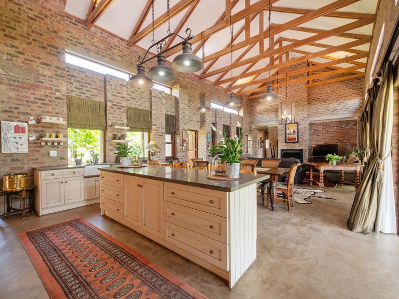 Spacious open-plan living area featuring exposed brick walls, high vaulted timber ceilings, a large kitchen island, and a cozy fireplace.