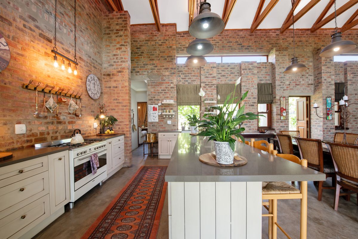 Spacious kitchen featuring exposed brick walls, timber ceiling beams, a large central island with stone countertops, and high-end gas range appliances.
