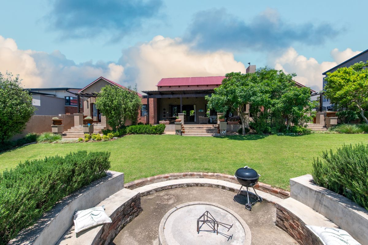 Spacious rear garden featuring a built-in circular fire pit, manicured lawn, and a covered patio area attached to the main residence.