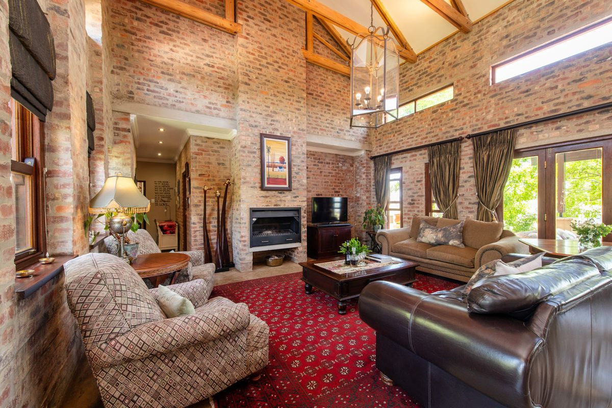 Spacious living room featuring high vaulted ceilings with exposed timber beams, striking brick feature walls, and a built-in fireplace with natural light.