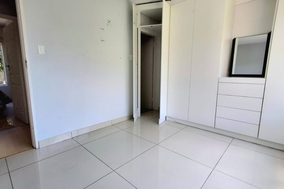 A vacant bedroom featuring white tiled flooring and built-in cupboards with a missing door panel, requiring minor wall repairs.