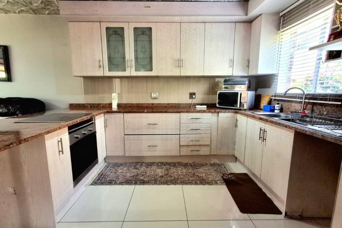A functional U-shaped kitchen featuring light wood-grain cabinetry, granite countertops, built-in oven, hob, and a double sink with a window view.
