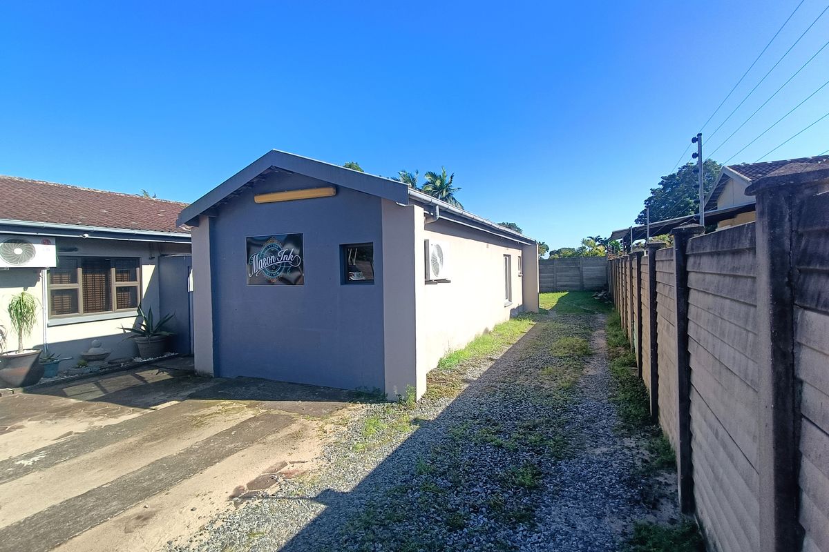 Rear exterior view of the property featuring a gravel driveway, concrete boundary wall, and external air conditioning unit.