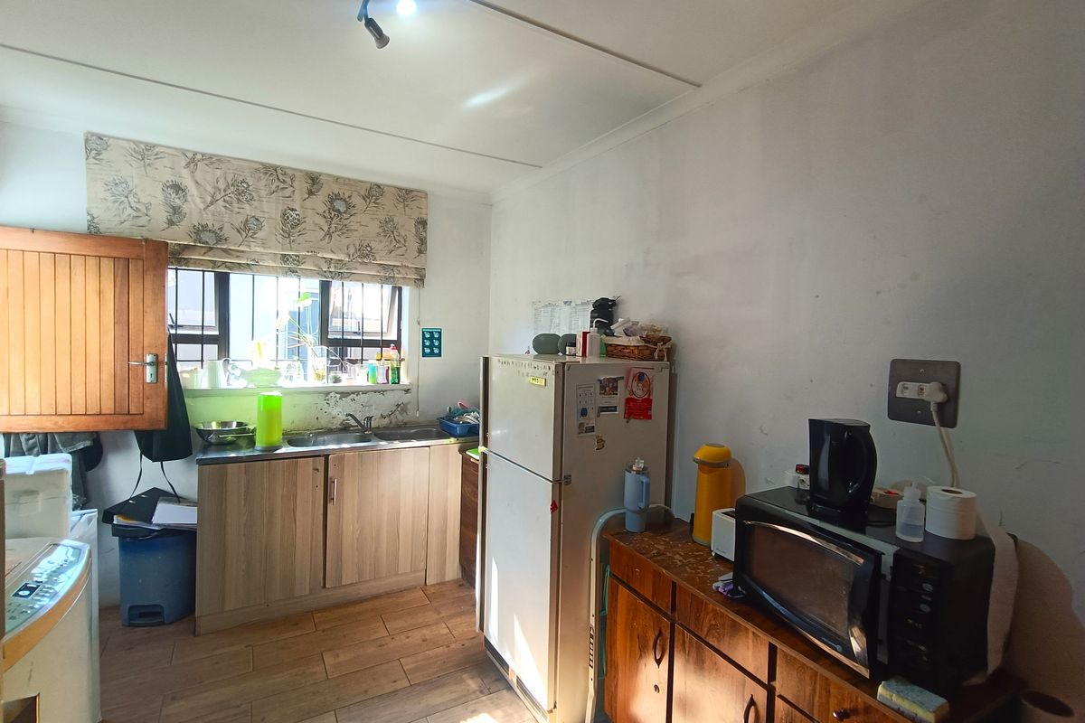 A functional kitchen area featuring laminate cabinetry, a stainless steel sink, and tiled flooring, currently showing signs of wear and maintenance needs.