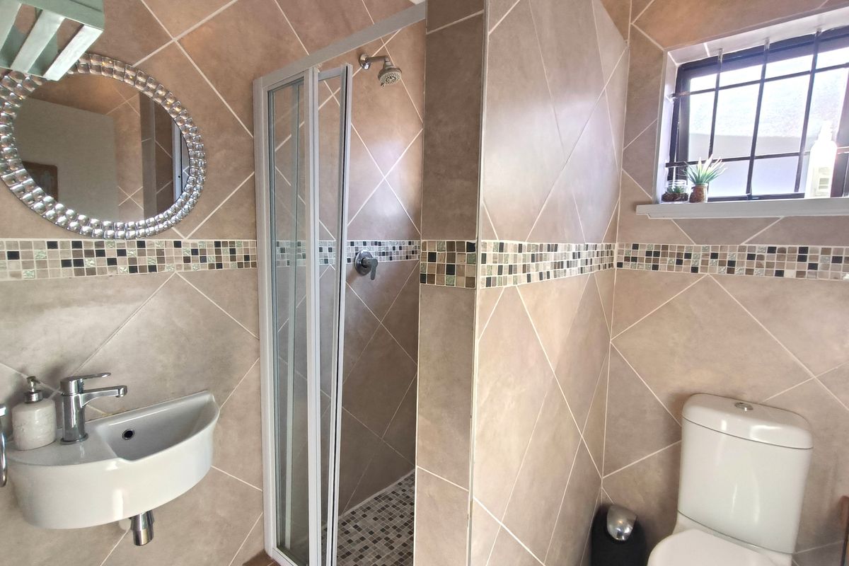 Compact bathroom featuring a shower enclosure, wall-mounted basin, and toilet, finished with neutral diamond-patterned wall tiles and a decorative mosaic border.