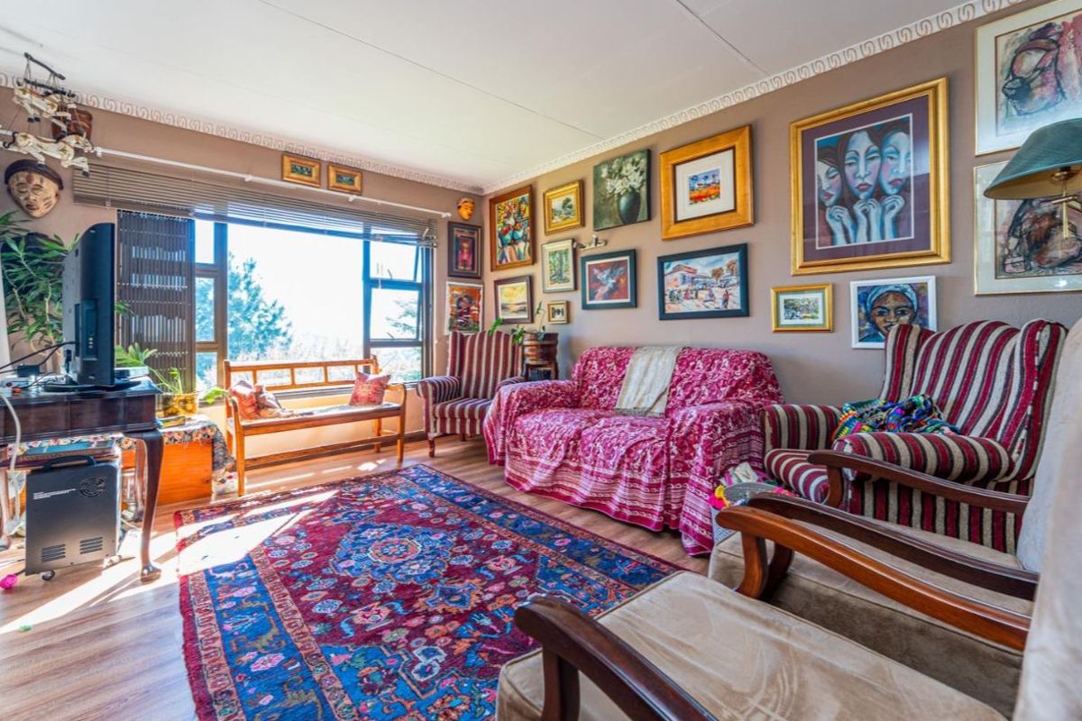 A well-lit living room featuring laminate flooring, decorative ceiling cornicing, and a large window providing natural light.