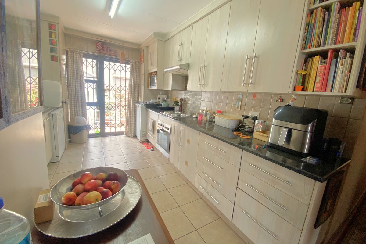 A functional galley-style kitchen featuring light wood-grain cabinetry, dark granite countertops, tiled flooring, and direct access to an outdoor area via a security gate.