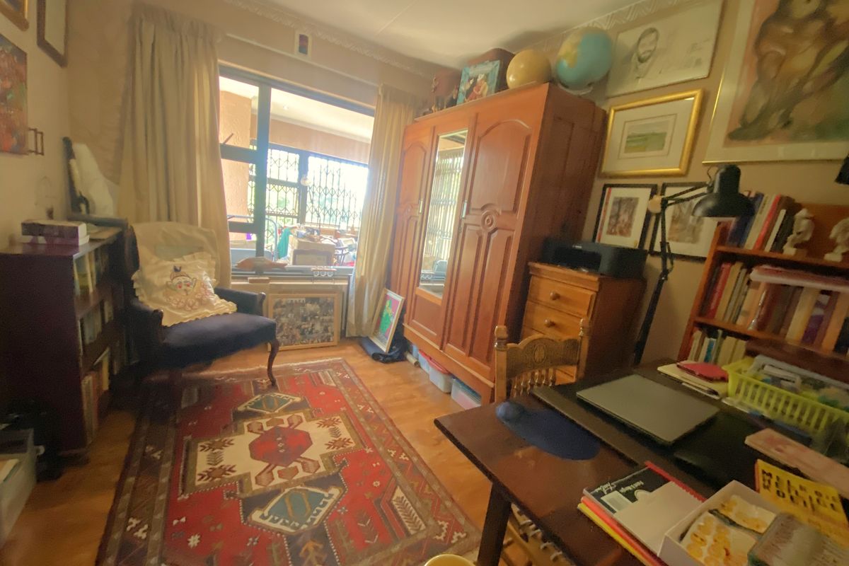 A multi-purpose room featuring laminate flooring, crown molding, and a large window with security bars, providing natural light and access to an outdoor area.