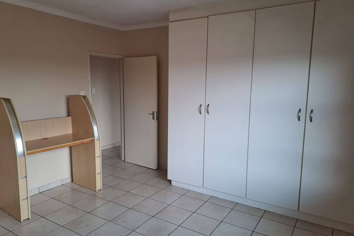 A spacious bedroom featuring neutral wall tones, tiled flooring, and ample built-in cupboard storage.