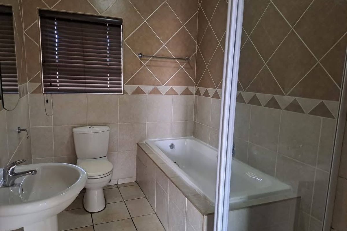 A functional bathroom featuring a pedestal basin, toilet, and a built-in bathtub with a shower enclosure, finished with neutral wall and floor tiling.