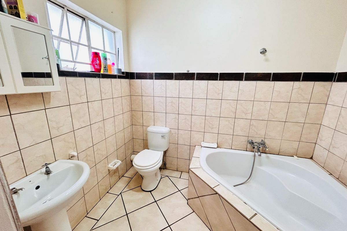 A functional bathroom featuring a pedestal basin, toilet, and corner bathtub with tiled finishes throughout.