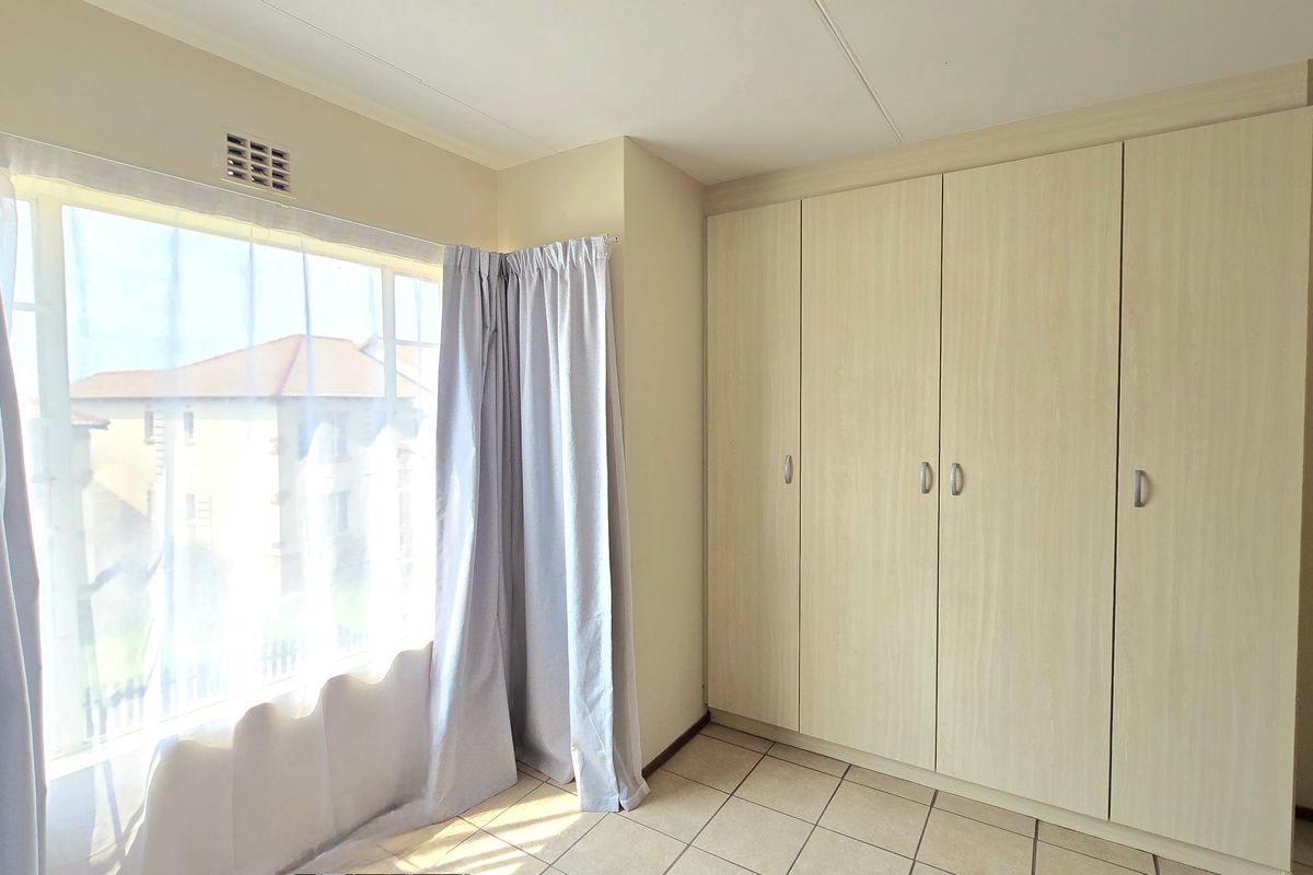 A bright and spacious bedroom featuring neutral tiled flooring and extensive built-in cupboard storage, offering a clean and functional living space.
