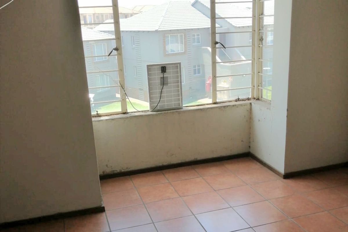 An empty living area featuring tiled flooring and large windows with security bars, showing signs of wear and requiring cosmetic updates.