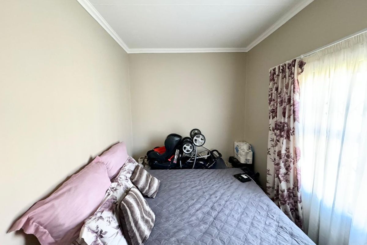 A compact bedroom featuring neutral wall tones, crown molding, and a window with installed curtain rails.