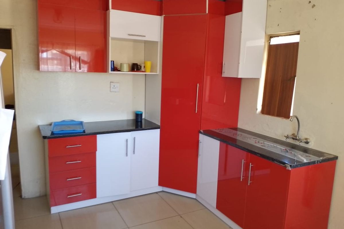 A compact kitchen featuring modern red and white high-gloss cabinetry, dark stone countertops, and a stainless steel sink.