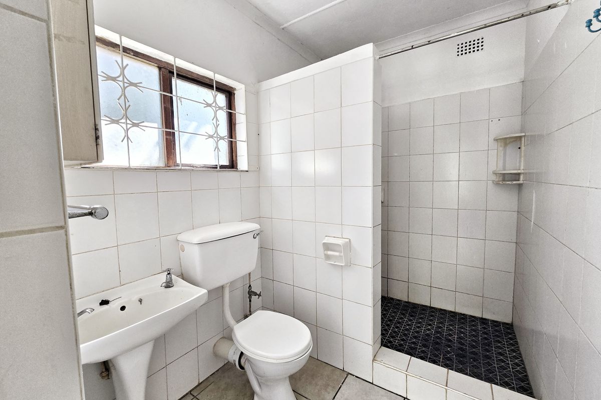 A functional bathroom featuring a pedestal basin, toilet, and a walk-in shower with tiled finishes, ready for modernization.