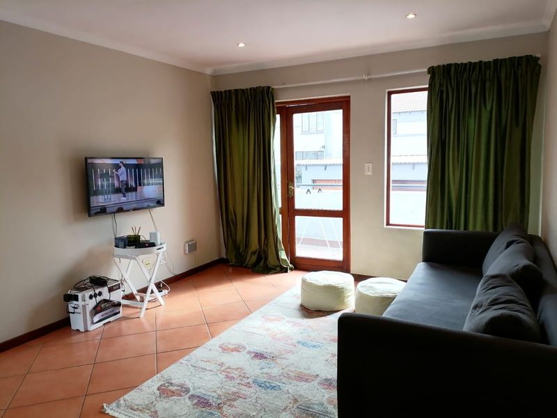 A living room featuring terracotta floor tiles, recessed ceiling lighting, and a glass-paneled door providing access to an outdoor balcony area.