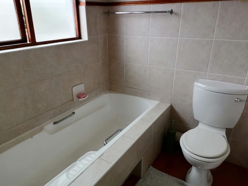 A functional bathroom featuring a built-in bathtub with chrome grab rails, a standard toilet, and neutral wall tiling.