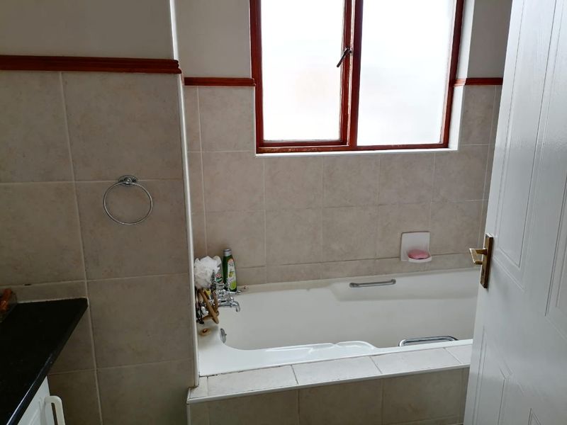A functional bathroom featuring a built-in bathtub with tiled surround, chrome fixtures, and a window providing natural light.