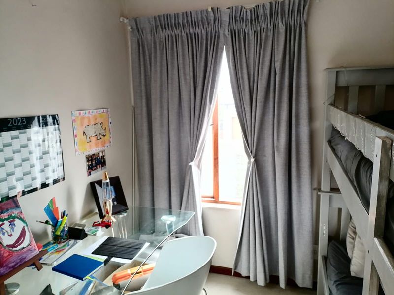 A bedroom featuring a window with grey curtains, providing natural light and space for a study area.